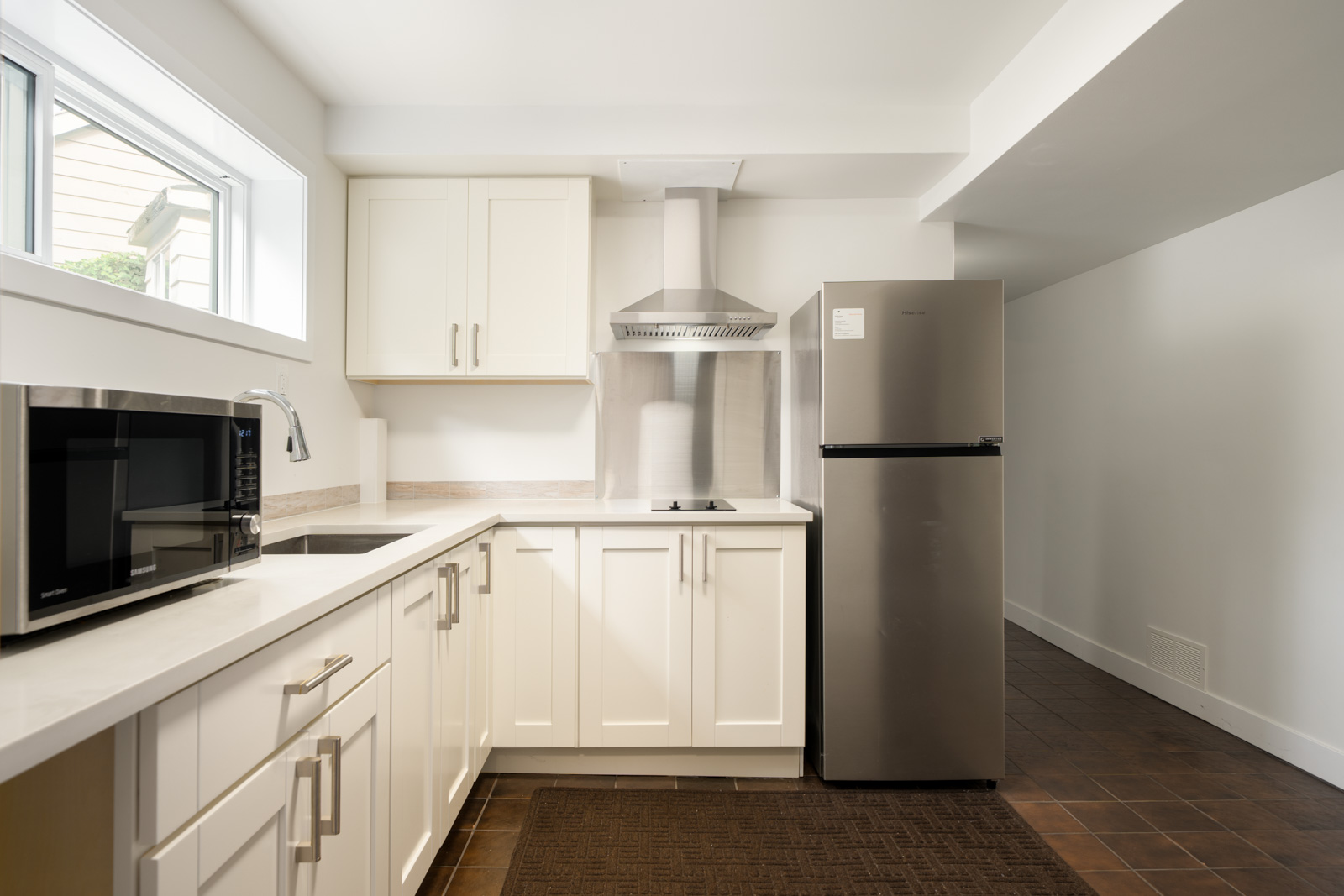 Kitchen at the Paton Street Vancouver basement with white cabinets, stainless steel appliances, and dark tiled flooring.