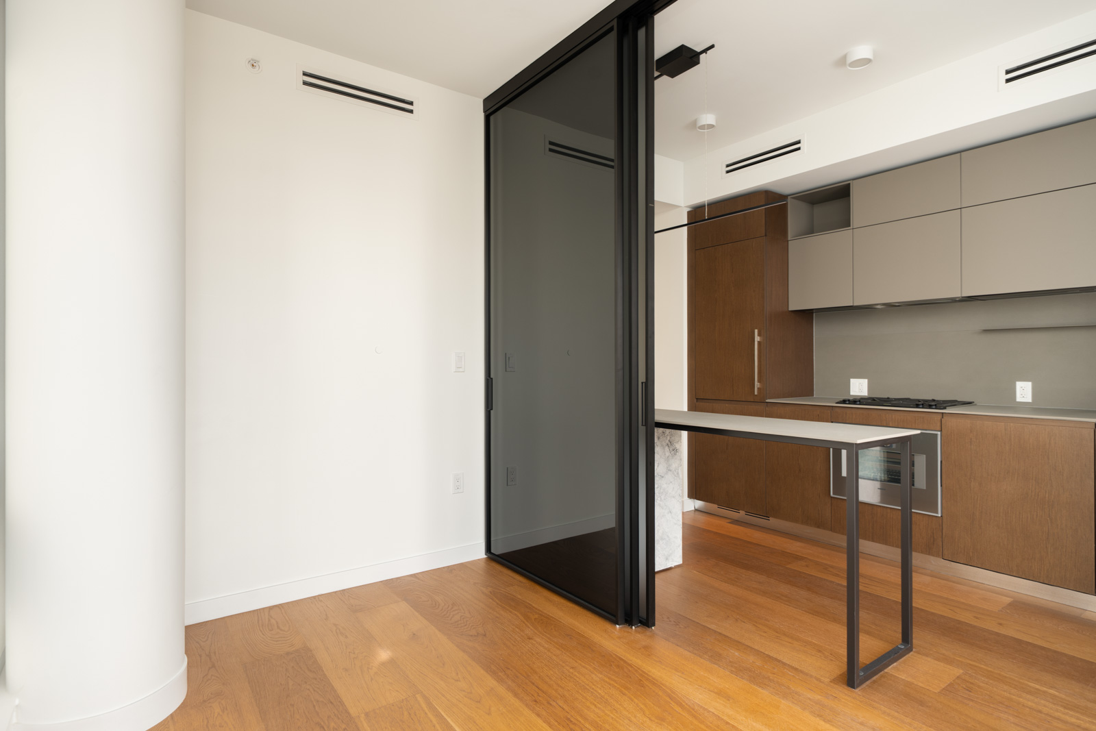 Kitchen at 1277 Hornby St featuring wood and gray cabinetry, a black sliding glass divider, and a narrow stone island.