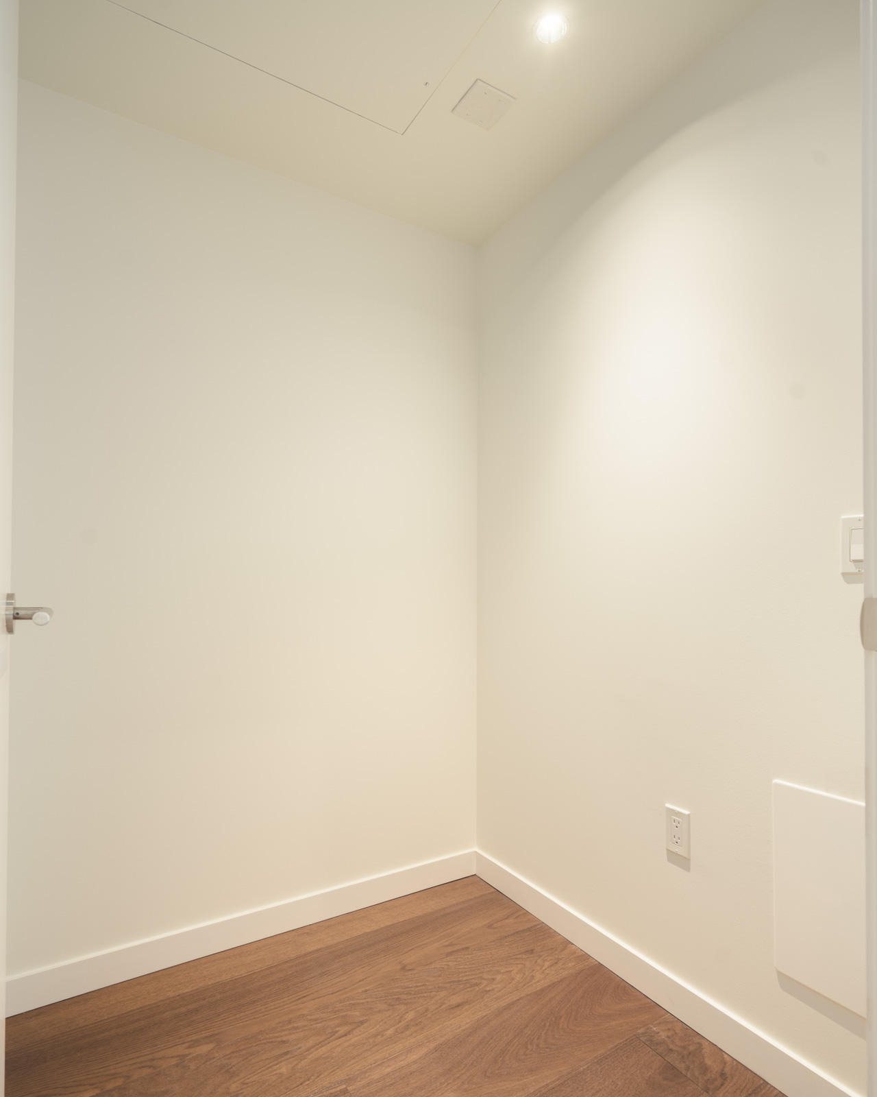 Empty corner of a 14th-floor Vancouver office with white walls, wood floors, a light switch, and an outlet.