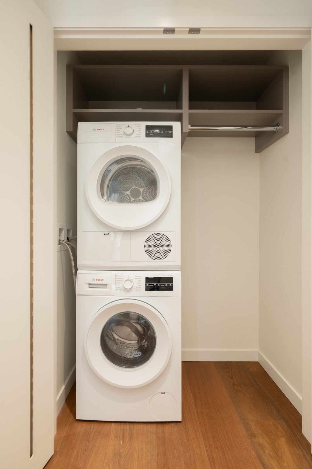 Stacked Bosch washer and dryer in a white closet with a shelf and hanging rod at a 14th-floor Vancouver office.
