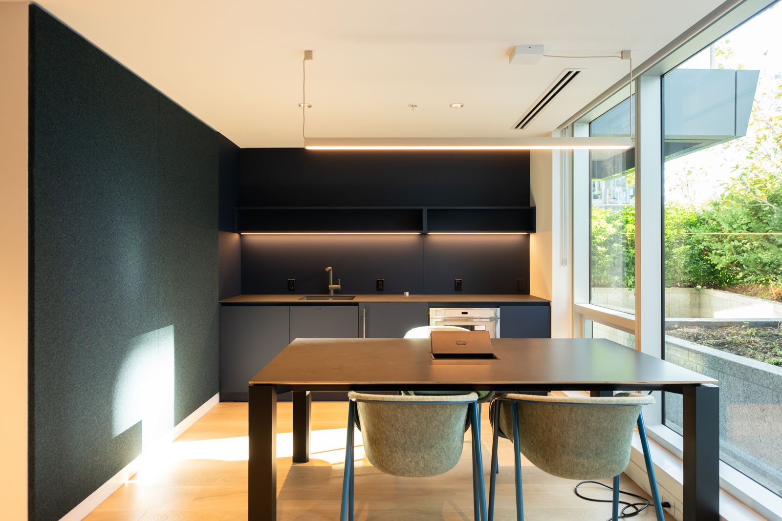 Modern kitchen in a 14th-floor Vancouver office with a dark workspace, island, two chairs, and windows overlooking greenery.