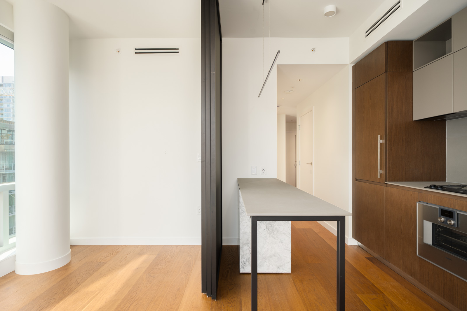 Modern kitchen at 1277 Hornby St featuring wood cabinetry, a marble-base island, a black room divider, and hardwood flooring.