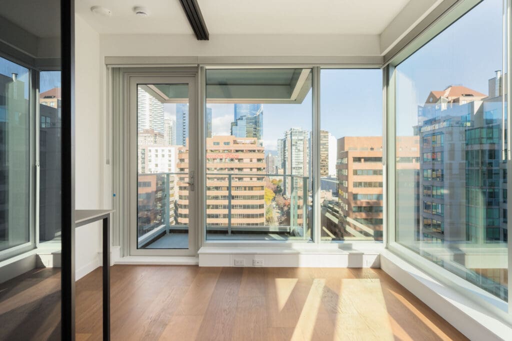 Empty room with hardwood floors and floor-to-ceiling windows overlooking the Vancouver skyline from the 14th floor.