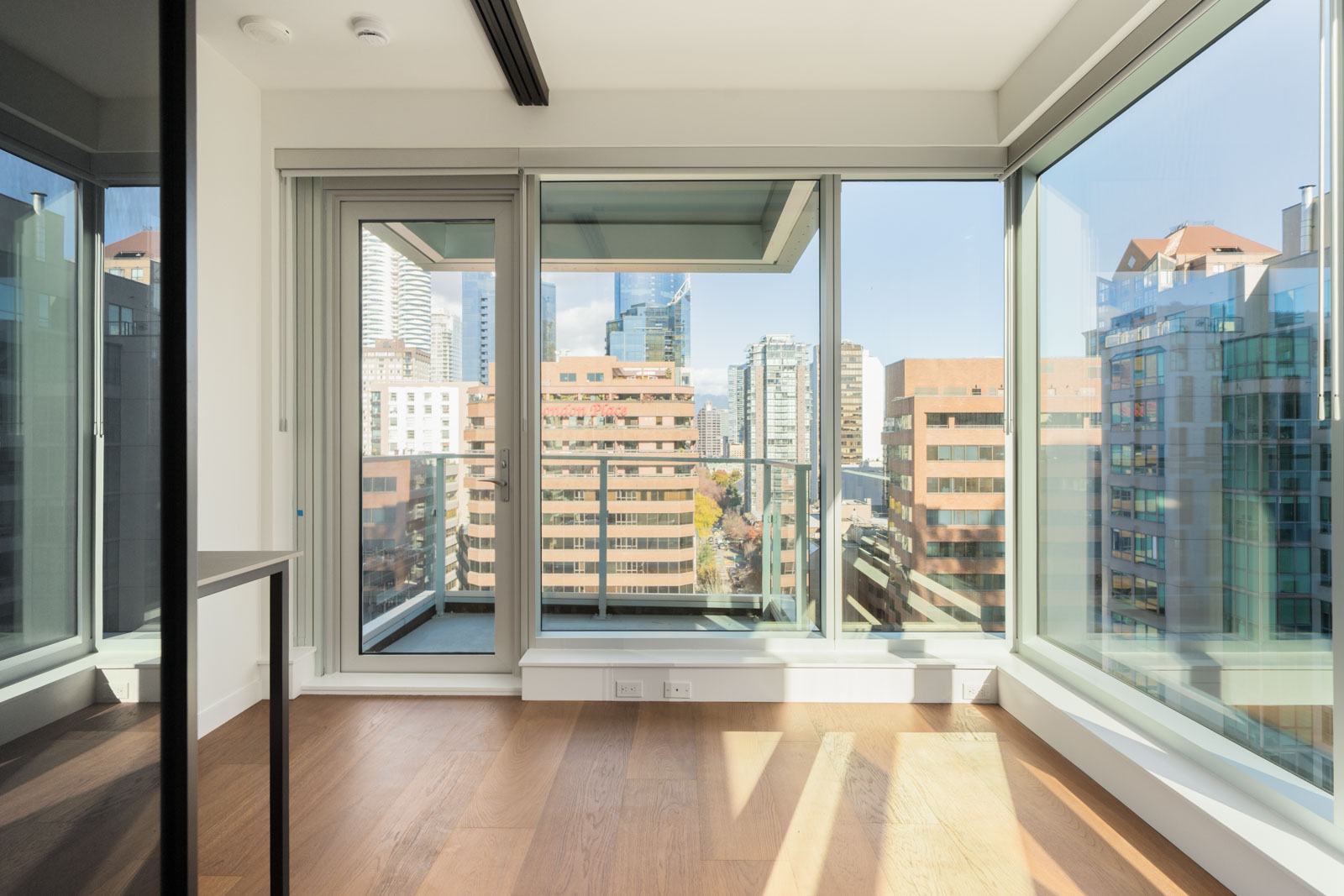 Empty room with hardwood floors and floor-to-ceiling windows overlooking the Vancouver skyline from the 14th floor.
