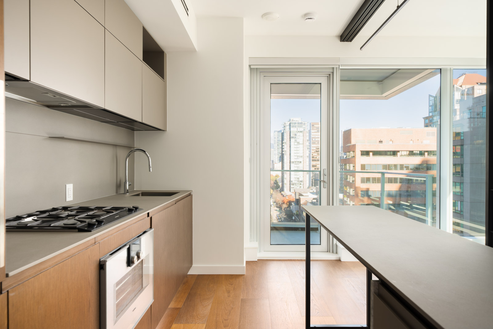 Modern kitchen with wooden cabinets, gas stovetop, and an island facing a balcony with a Vancouver city skyline view.