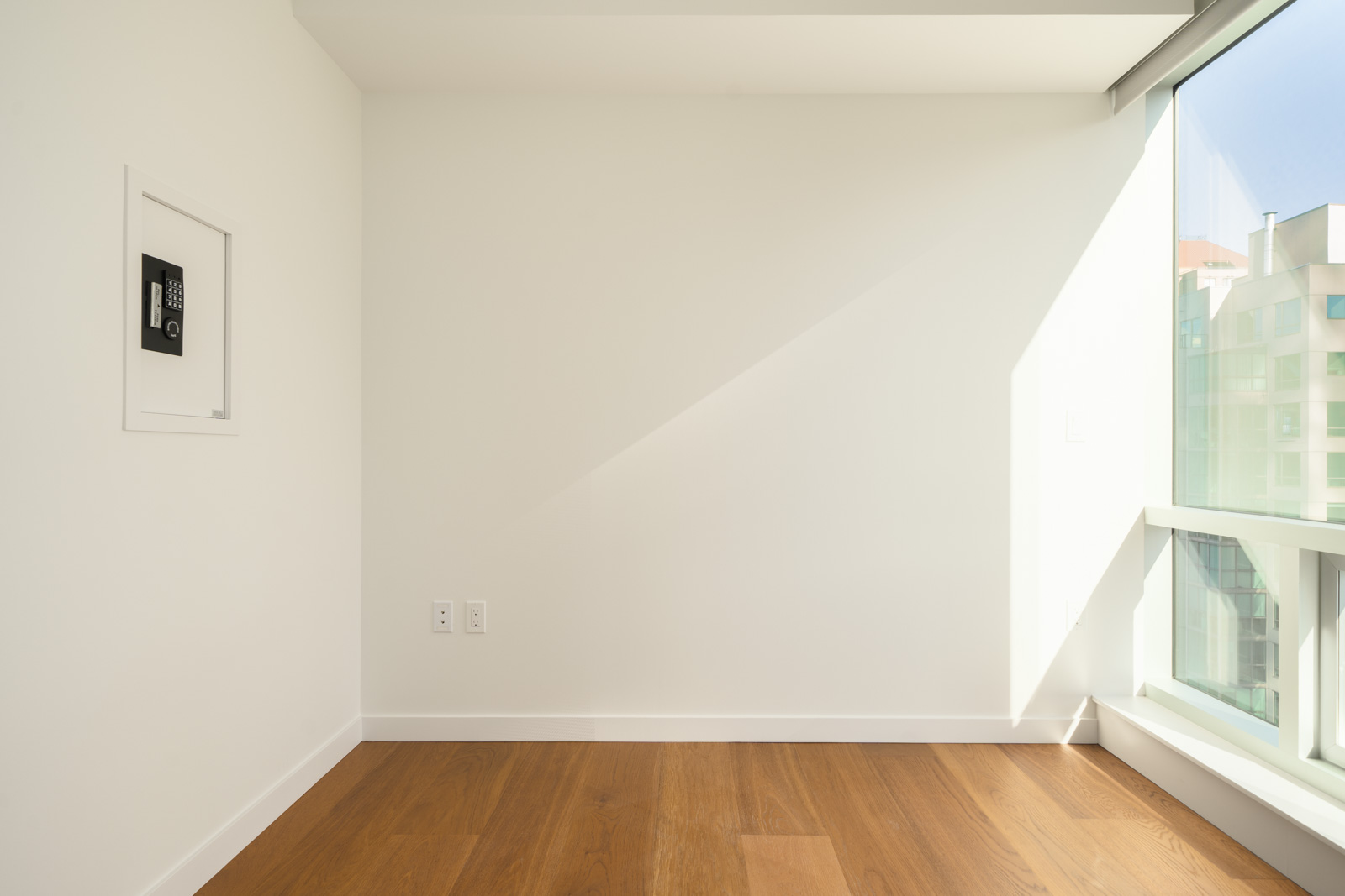 Empty room with wood floors, white walls, a security keypad, and a floor-to-ceiling window in a 14th-floor Vancouver office.