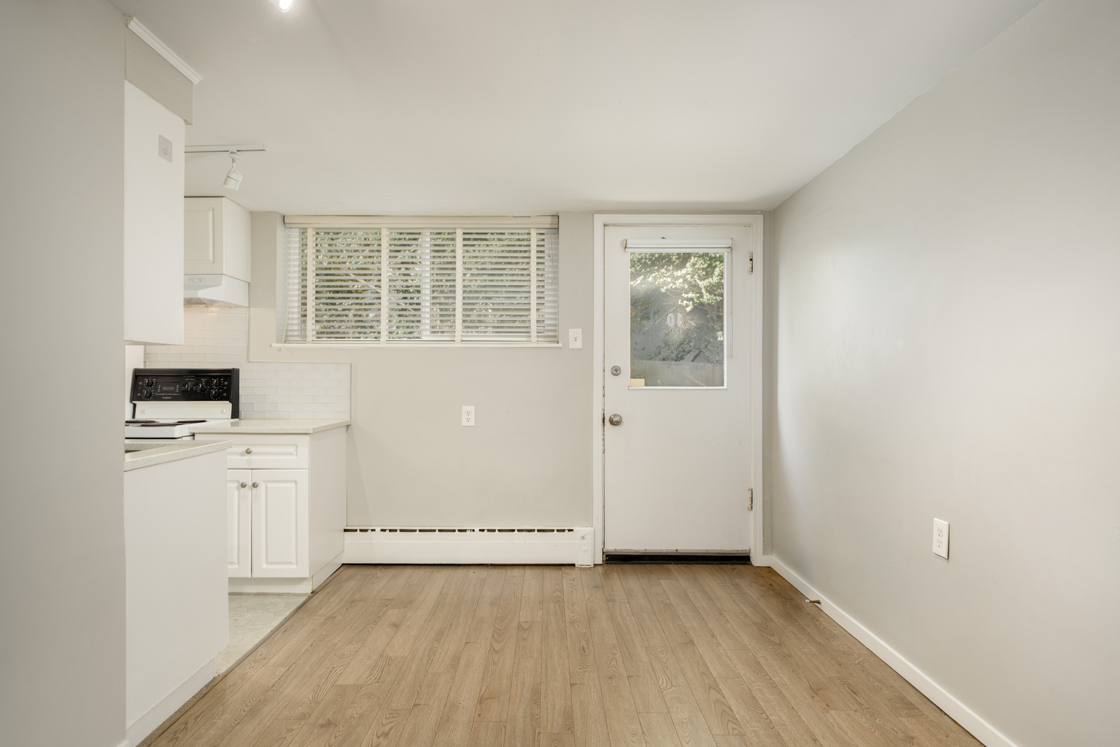Compact kitchen at 1445 W 11th Ave featuring white cabinets, a black stove, light wood-look flooring, and a white back door.