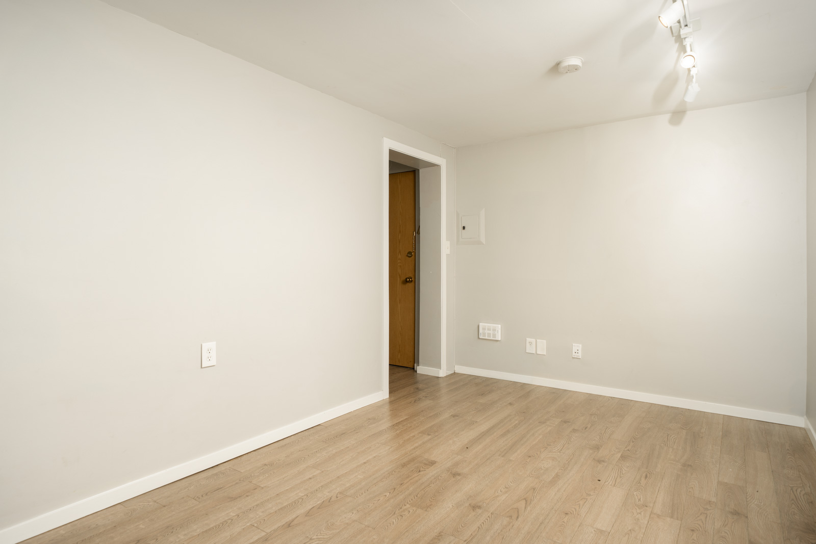 Empty room at 1445 W 11th Ave, Vancouver, featuring light gray walls, wood-look flooring, and a single wooden door.