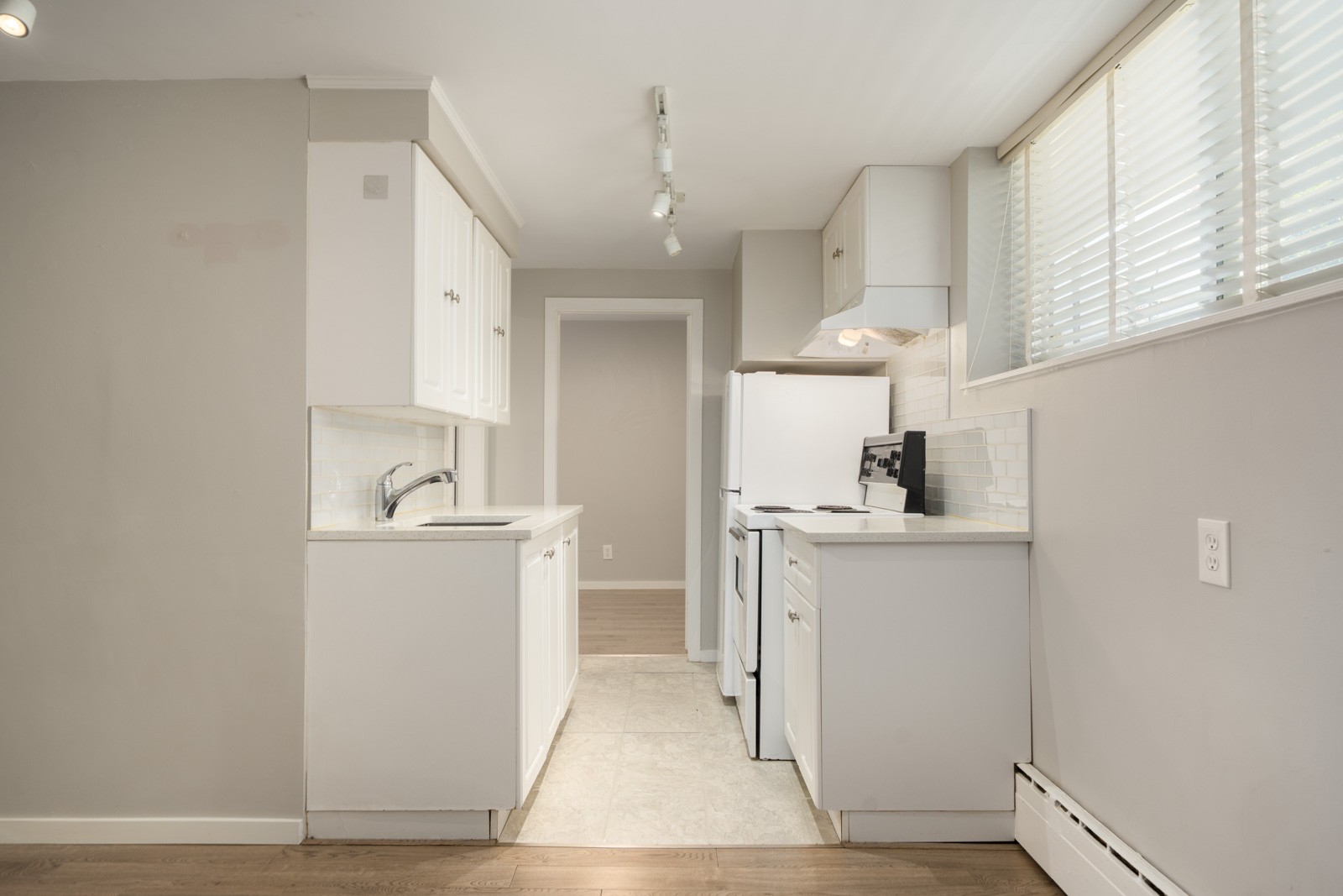Galley kitchen at 1445 W 11th Ave featuring white cabinets, white appliances, and a tiled backsplash.