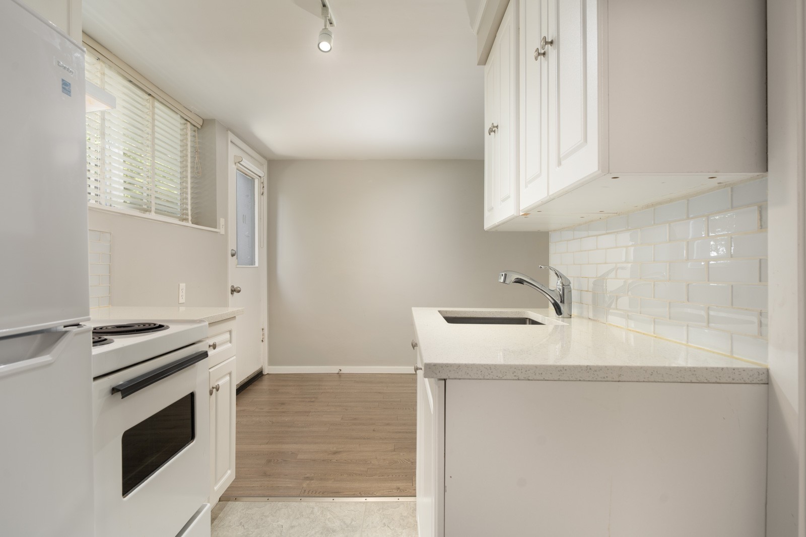 Kitchen at 1445 W 11th Ave with white cabinets, sink, stove, and a white door leading to an empty room.