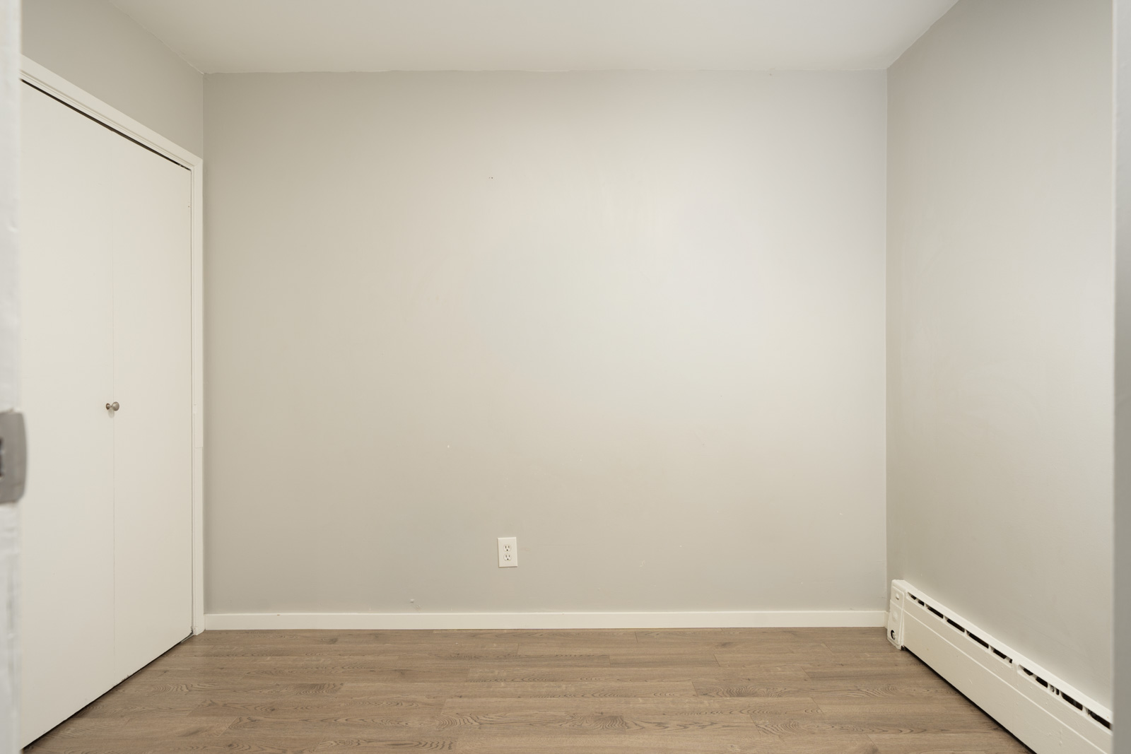 Empty room with light gray walls, wood-look floors, a white closet door, and a baseboard heater in a Vancouver property.