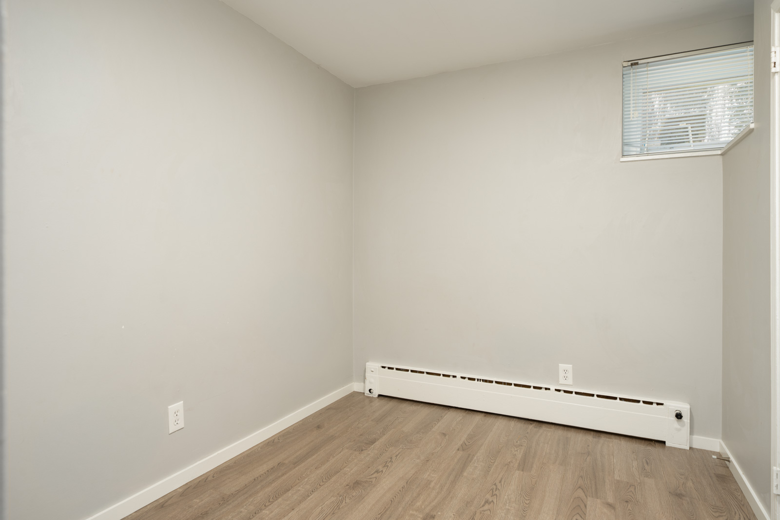 Empty room at 1445 W 11th Ave with light gray walls, wood-look flooring, and a window with blinds.