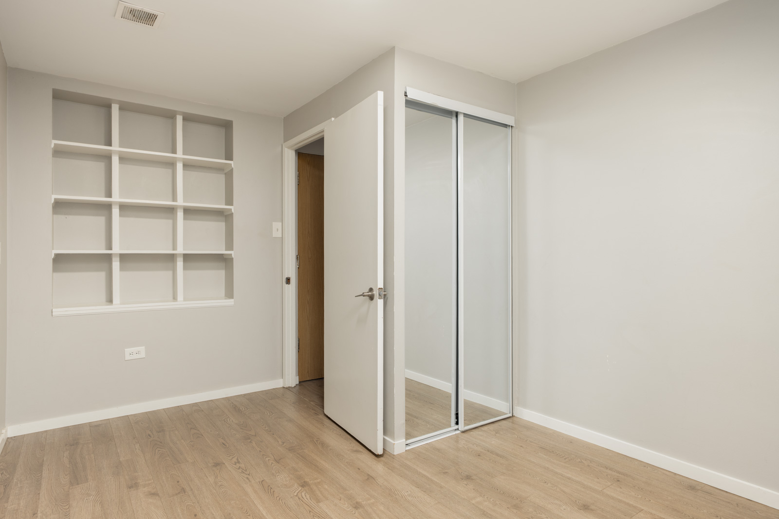 Room with light wood flooring, an open door, a mirrored sliding closet, and built-in shelves in a Vancouver listing.