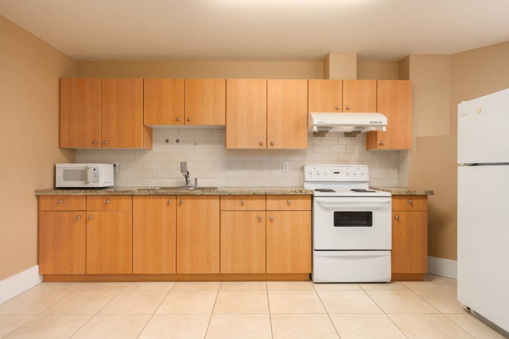 Kitchen with wood cabinets, light stone countertops, white appliances, and a tiled backsplash in a Vancouver basement.