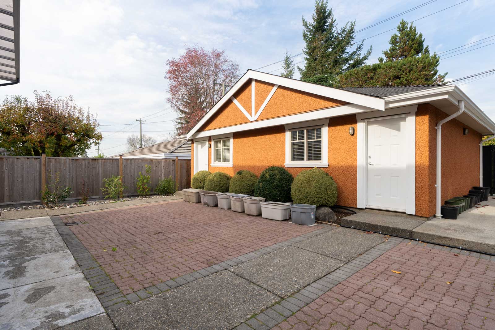 Orange stucco garage with two white doors and several planters in a Yew St paved driveway.