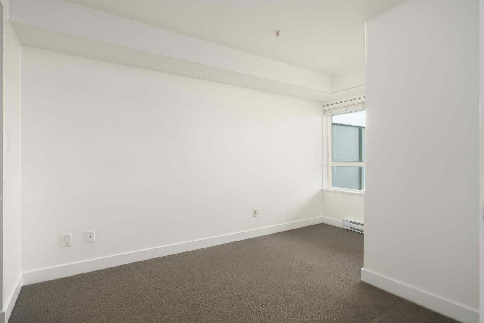 An empty 3rd-floor office in Vancouver featuring white walls, brown carpeting, and a window.