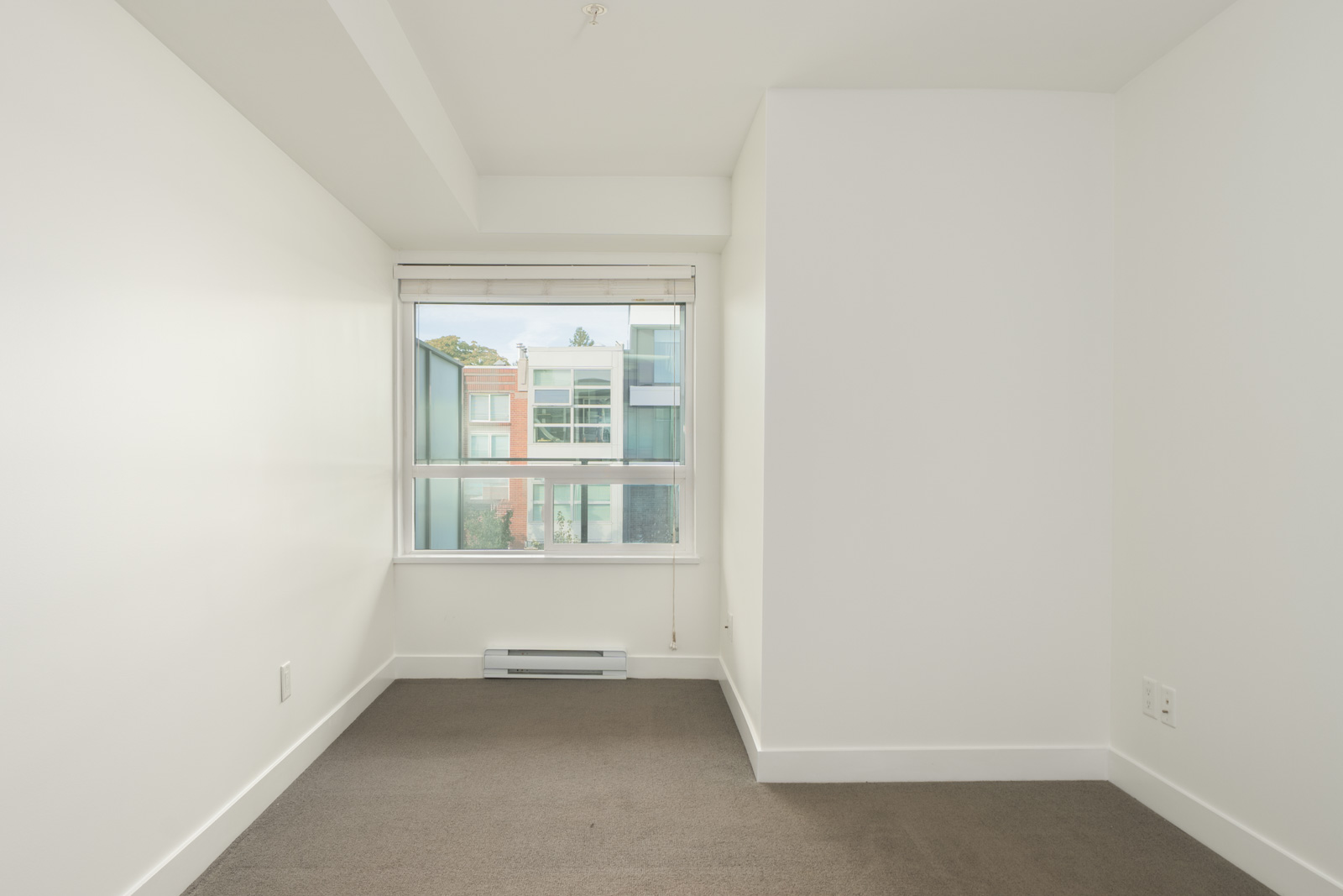 Empty 3rd-floor Vancouver office with white walls, grey carpet, and a large window overlooking neighboring buildings.