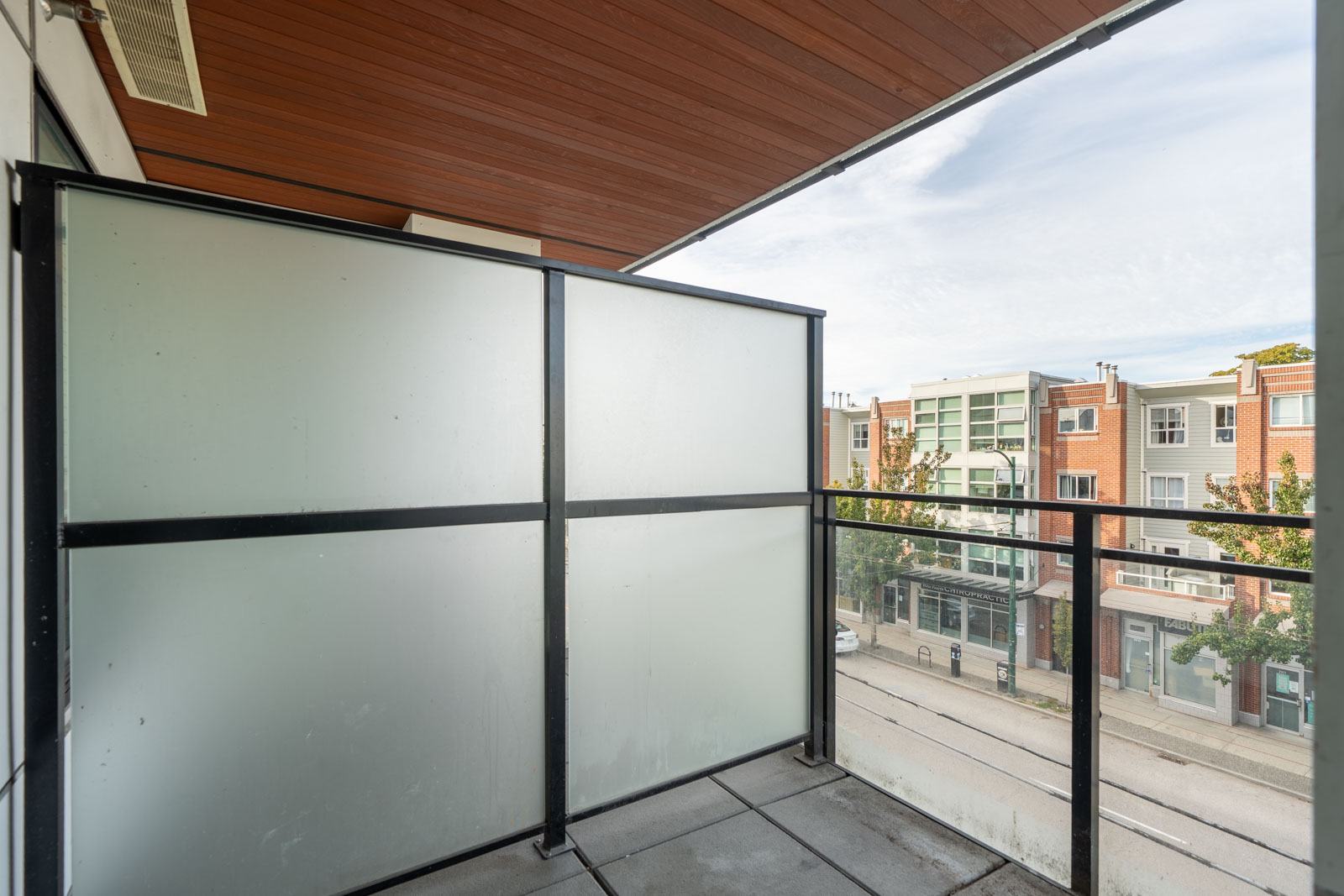 A 3rd-floor Vancouver balcony with a frosted glass privacy screen overlooking a city street and apartment buildings.