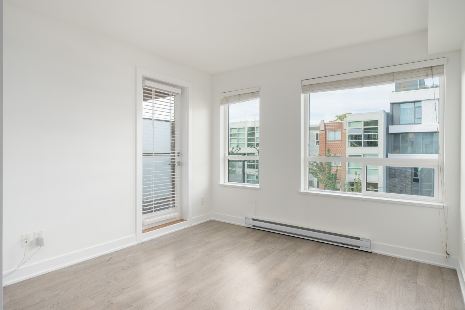 Empty 3rd-floor office in Vancouver with white walls, wood-look floors, a glass door, and urban window views.