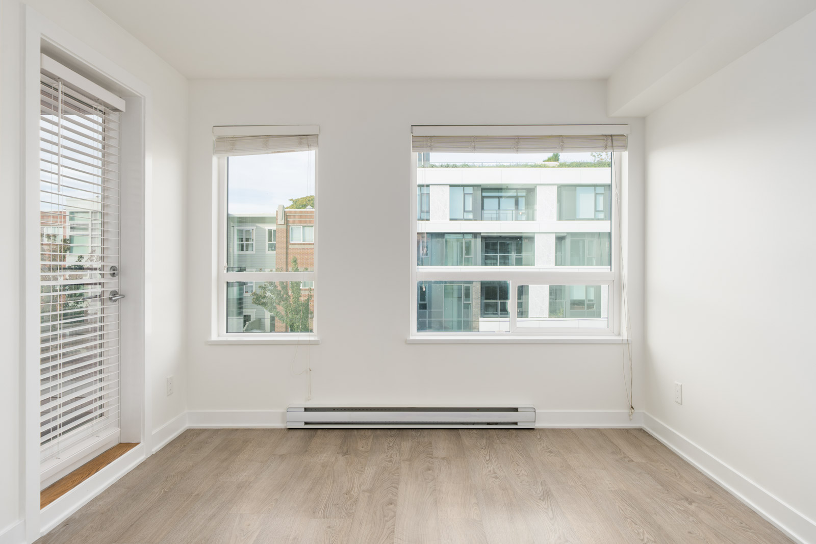 Empty 3rd-floor Vancouver office with white walls, wood-look flooring, two windows, and a glass door to a balcony.