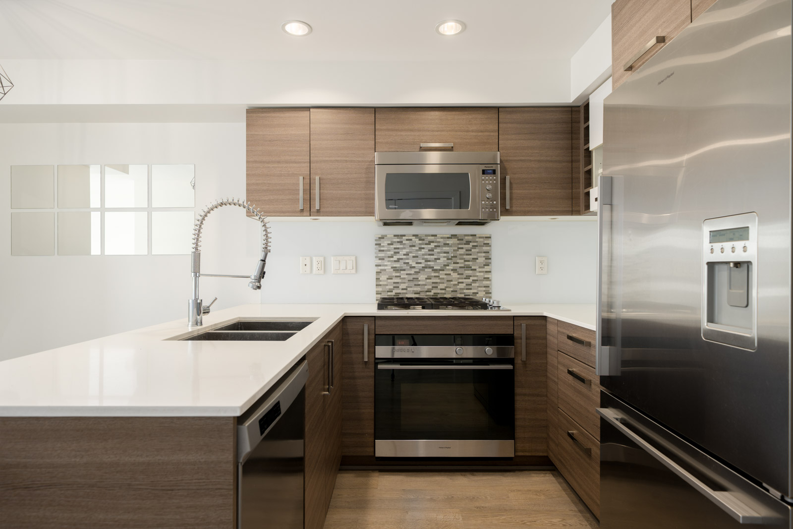 Modern kitchen in a Kitsilano commercial space featuring wood cabinets, stainless steel appliances, and a white countertop.