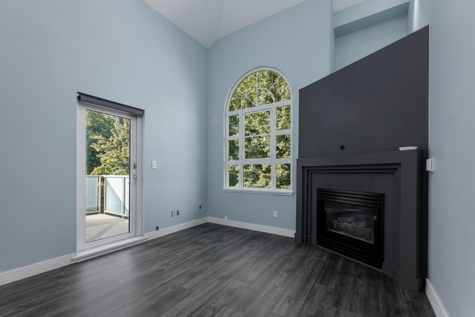 Modern living room on the 3rd floor at 2231 Welcher Ave, Port Coquitlam with gray floors, blue walls, arched window, and balcony.