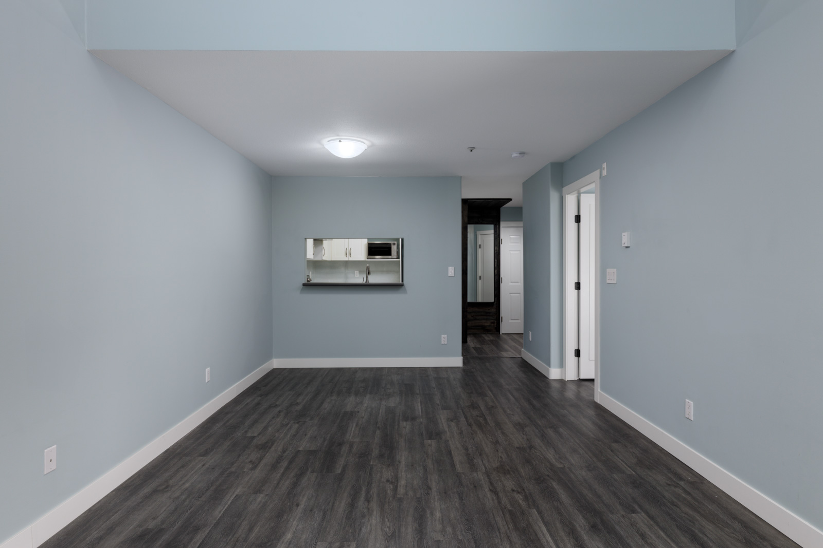 Empty room on 3rd floor at 2231 Welcher Ave, Port Coquitlam, with light blue walls, dark wood floors, and pass-through window.