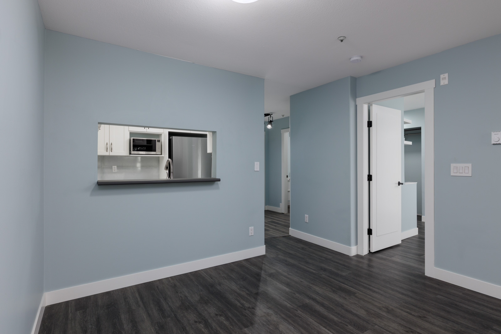 Empty 3rd floor room at 2231 Welcher Ave, Port Coquitlam; light blue walls, dark wood floor, open doorway, kitchen pass-through.