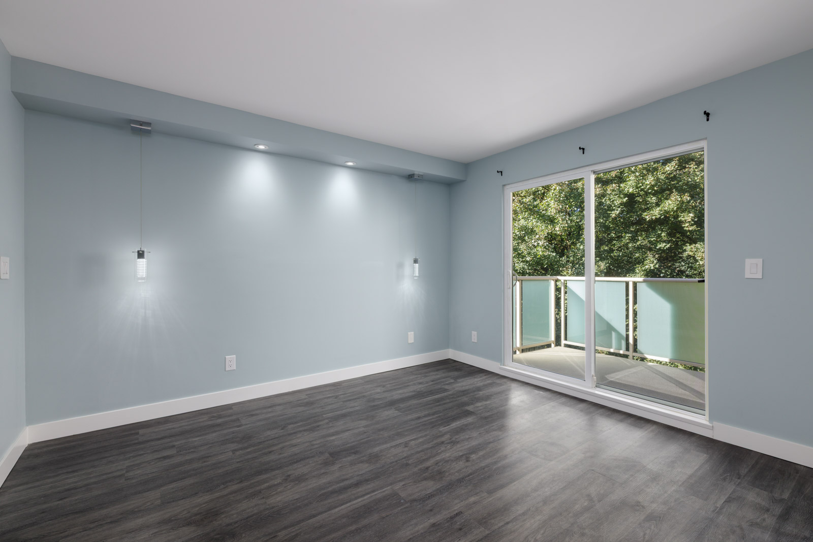 Bright, empty third-floor room at 2231 Welcher Ave, Port Coquitlam with light blue walls, dark wood floors, and glass balcony door.