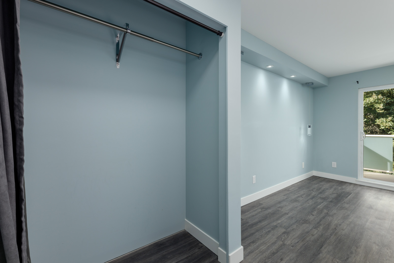 Empty room on 3rd floor at 2231 Welcher Ave, Port Coquitlam; blue walls, grey floor, open closet, and balcony with greenery.