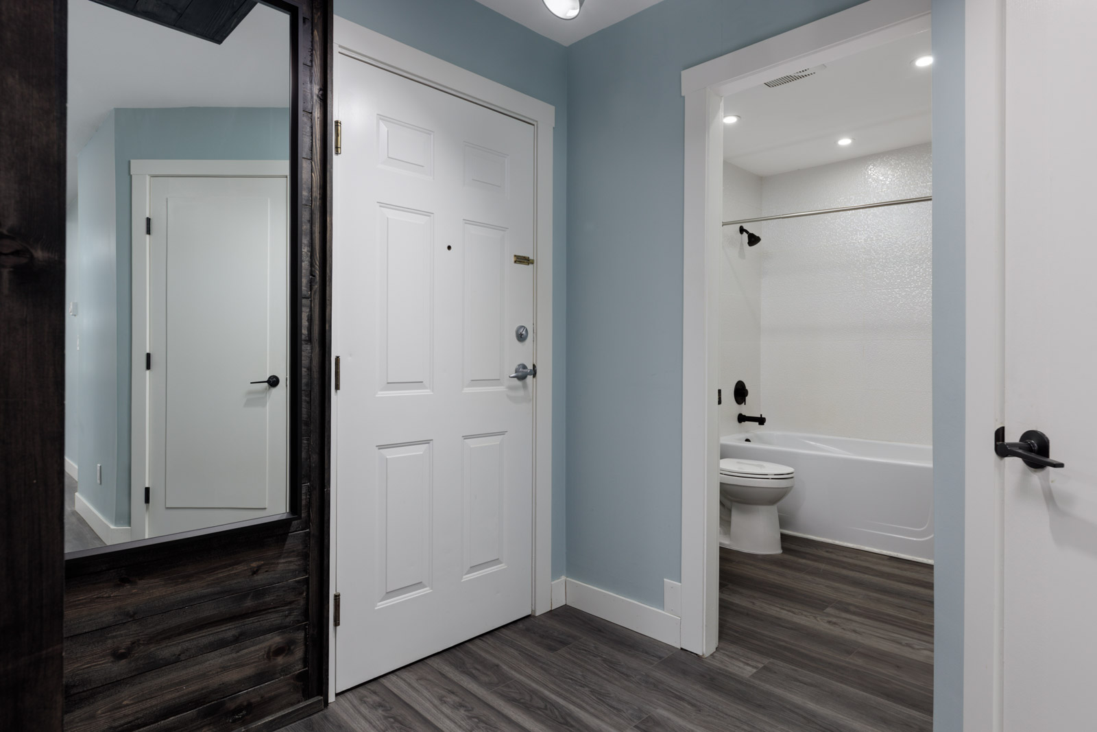 White front door, wood floors, large mirror, and bathroom view on the third floor at 2231 Welcher Ave, Port Coquitlam.