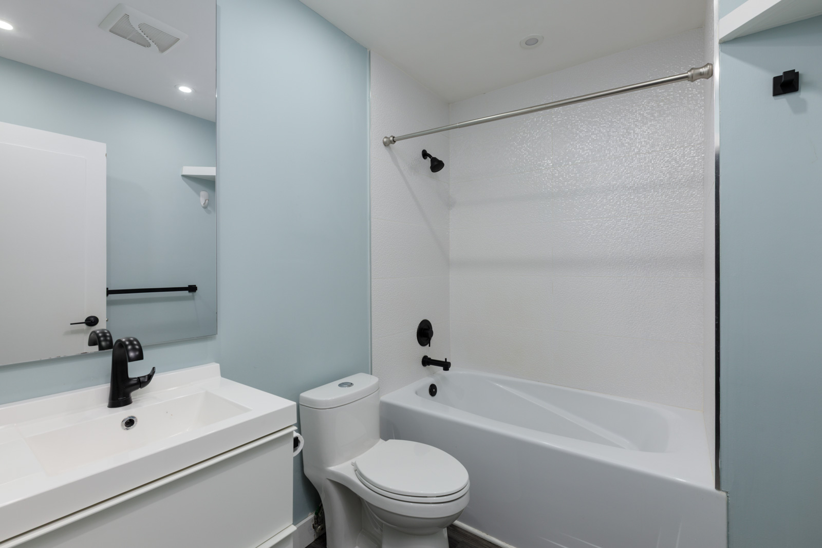 3rd floor bathroom at 2231 Welcher Ave, Port Coquitlam with light blue walls, black fixtures, white sink, toilet, tub, and mirror.
