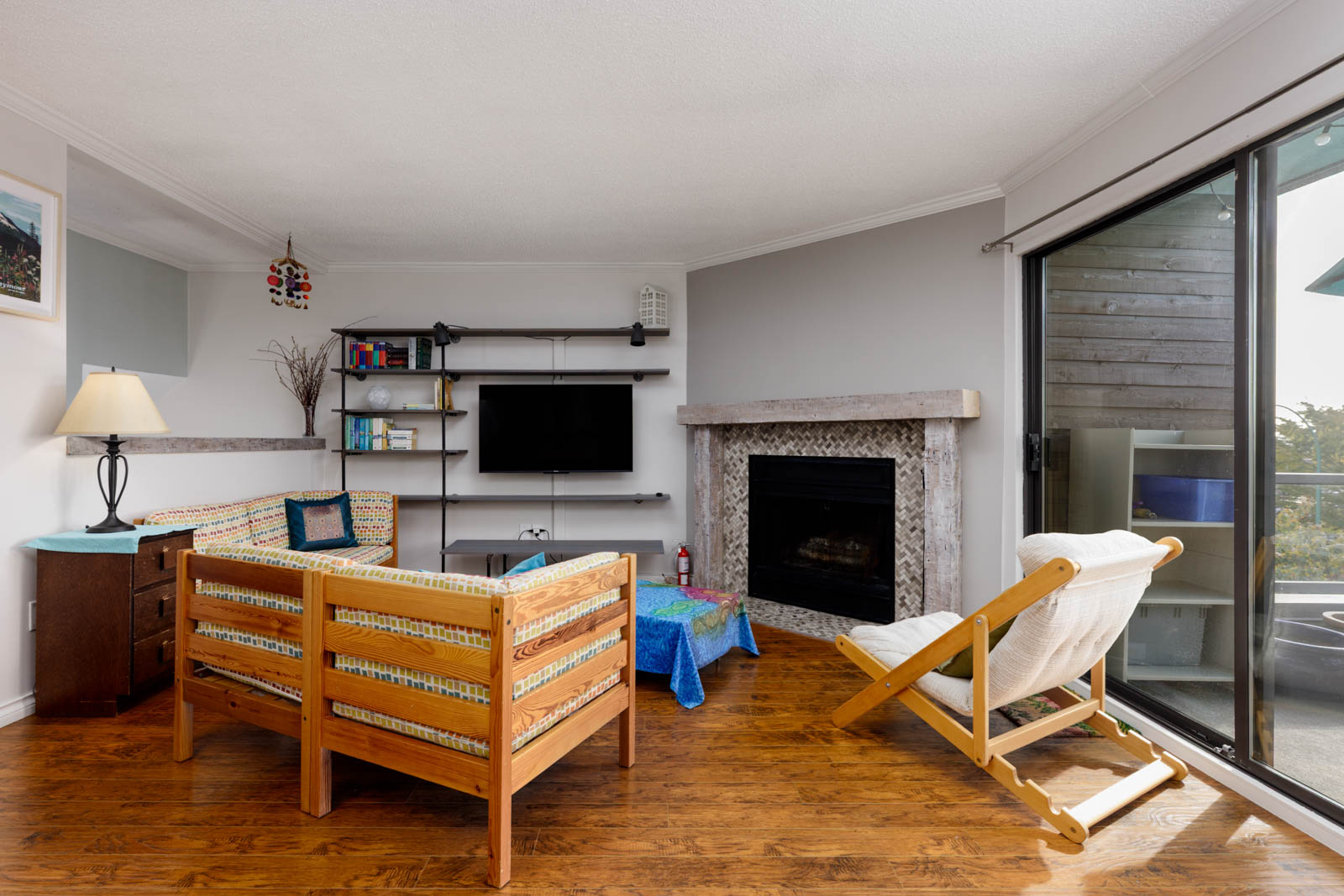 Living room of a North Vancouver townhouse with wooden floors, patterned sofa, fireplace, and sliding door to a balcony with chairs.