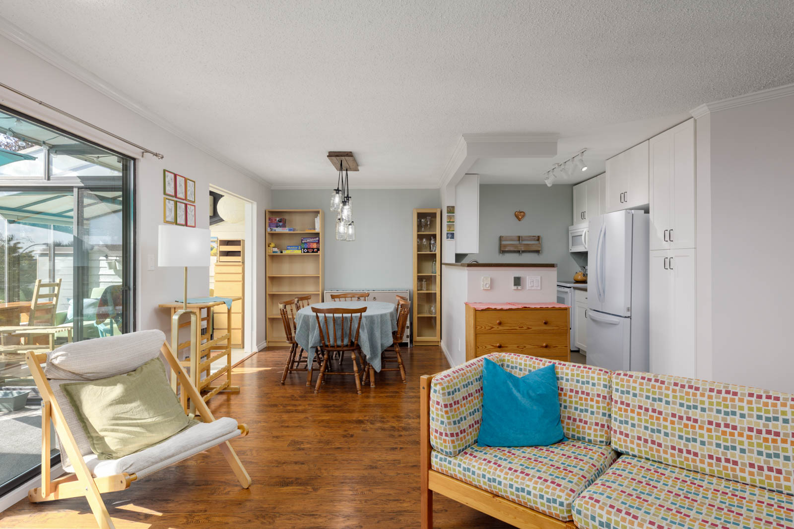 Townhouse kitchen and dining area at 220 4th St E, North Vancouver, with wood floors, colorful couch, chair, and sliding glass doors.