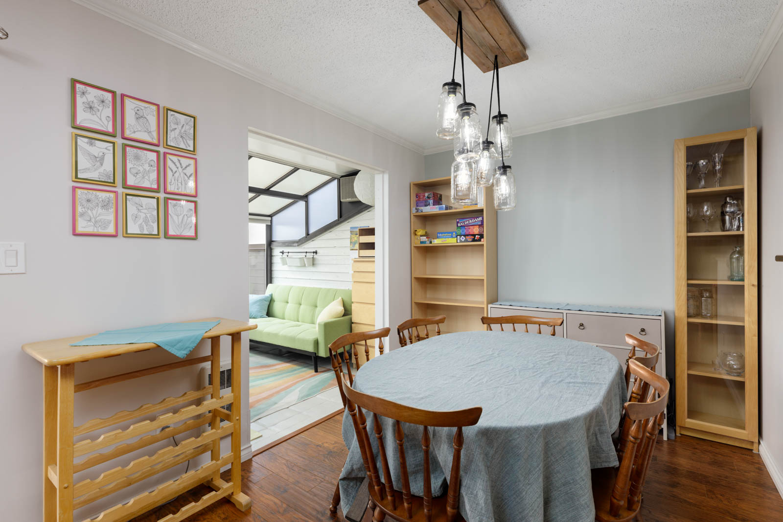 North Vancouver townhouse dining room with round table, wooden chairs, shelves of board games and glassware, view to sunroom.