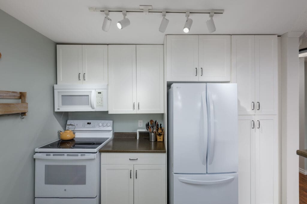 Modern kitchen in a North Vancouver townhouse at 220 4th St E with white cabinets, brown countertops, and track lighting.