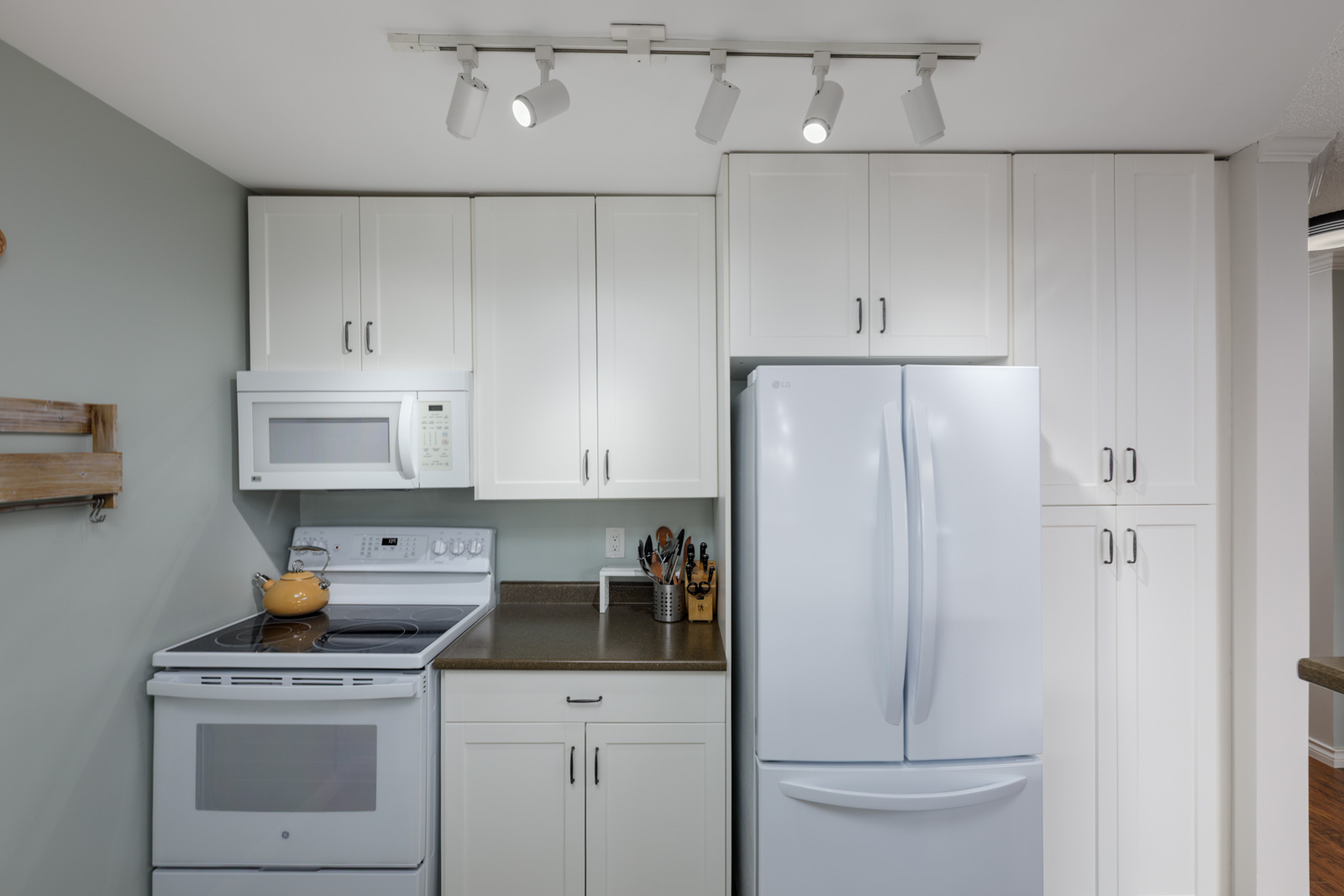 Modern kitchen in a North Vancouver townhouse at 220 4th St E with white cabinets, brown countertops, and track lighting.