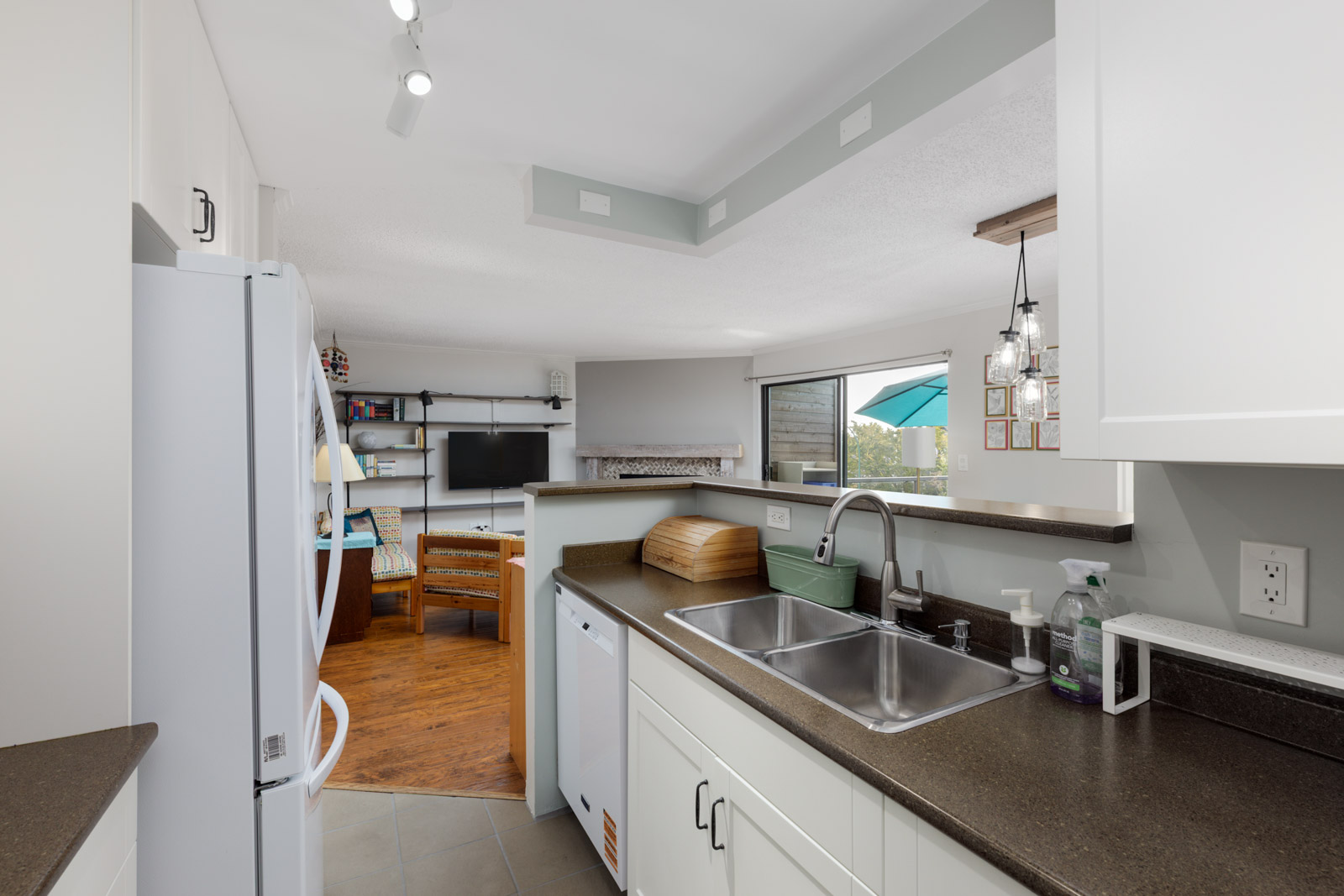 Modern kitchen with white cabinets, dark countertops, double sink, and a living room view at 220 4th St E, North Vancouver.