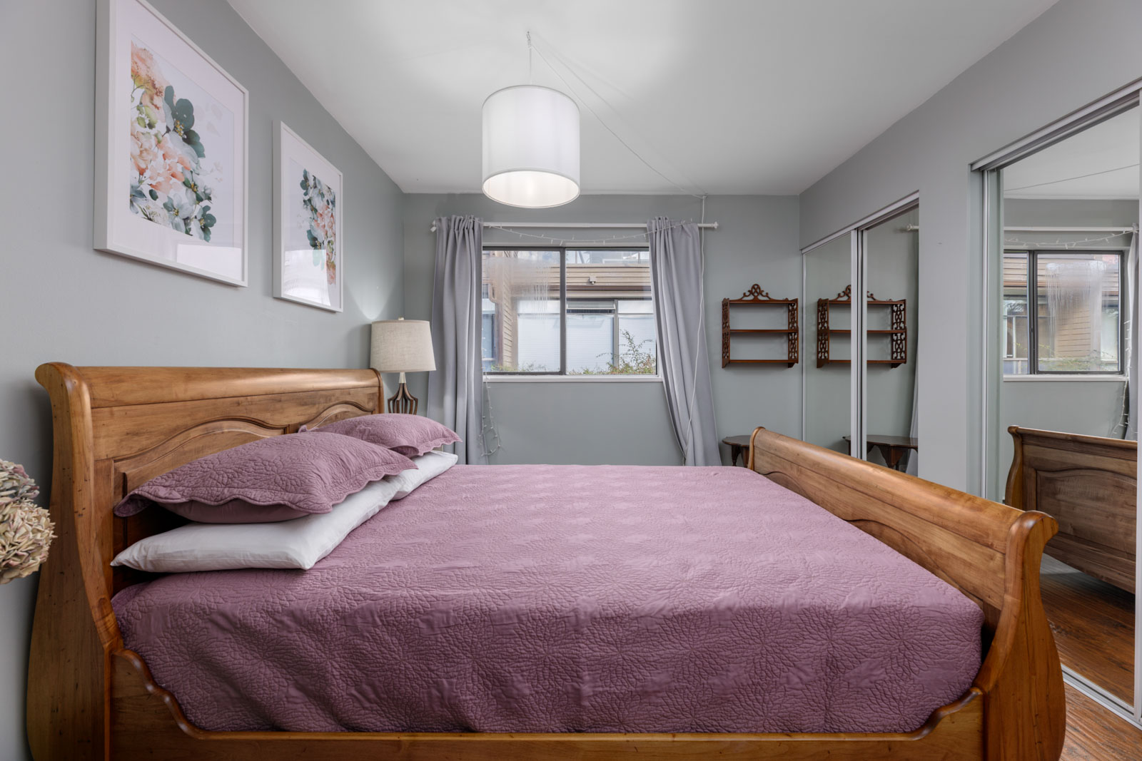 Townhouse bedroom at 220 4th St E, North Vancouver with wooden bed frame, mauve quilt, floral art, large windows, mirrored closet.