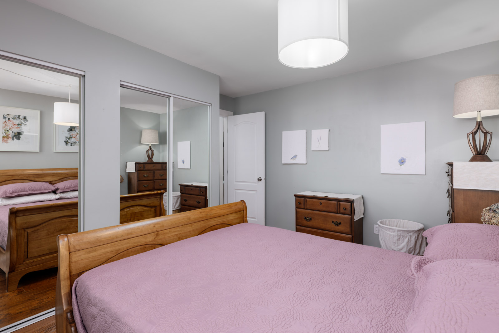 Cozy North Vancouver townhouse bedroom with a wooden bed, lavender bedding, mirrored closets, nightstands, and framed art.