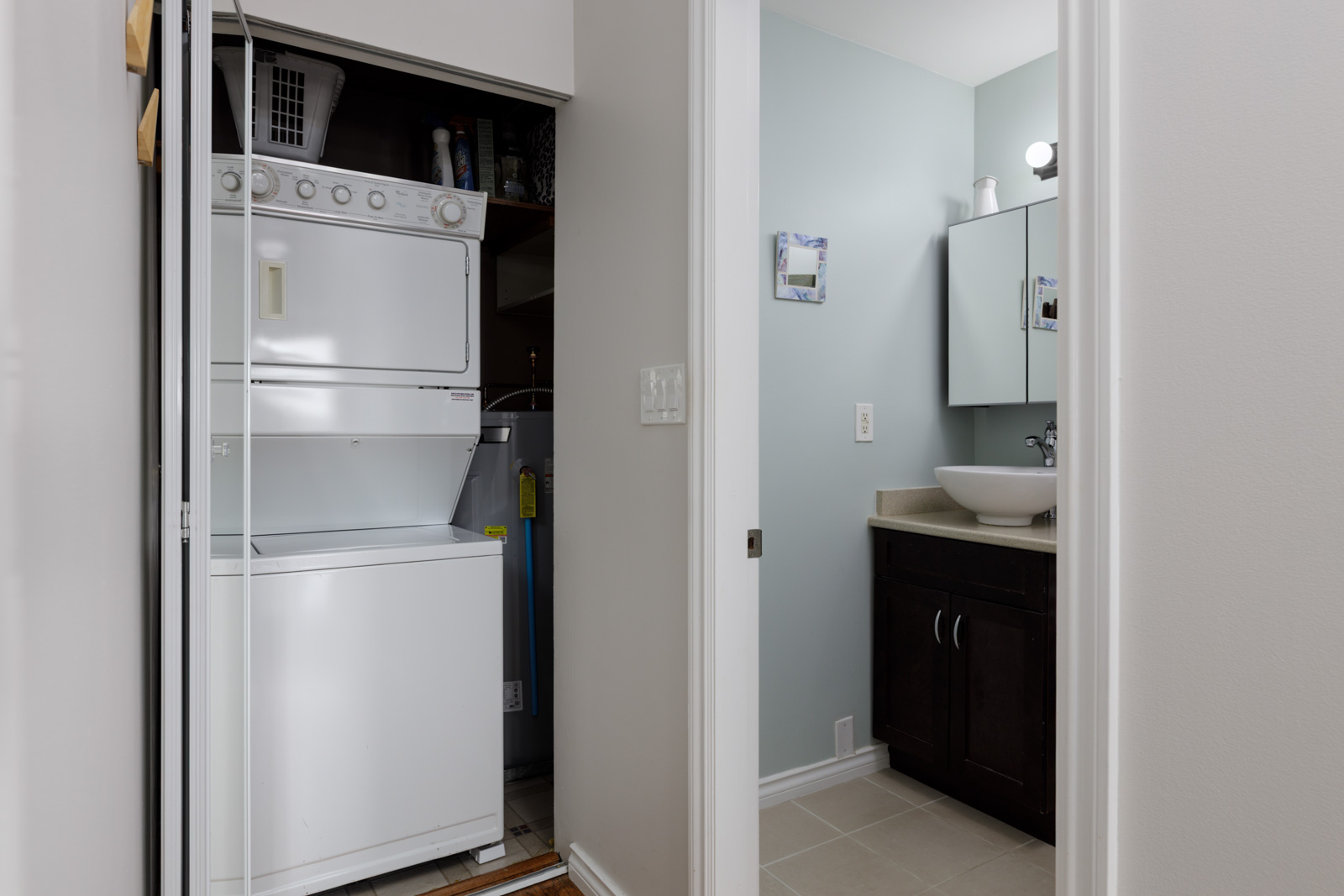 Stacked washer and dryer in a closet near an open door to a bathroom with sink, mirror, and cabinet in North Vancouver.