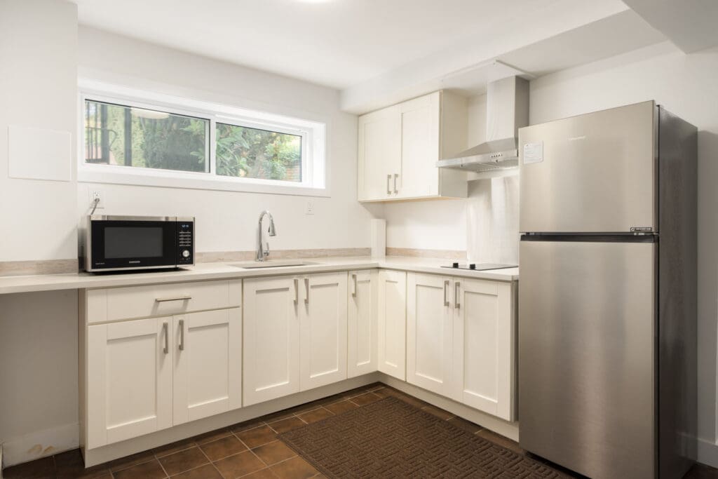 Kitchen with white cabinets, stainless steel appliances, a sink, and a window in a Haggart Street Vancouver basement.