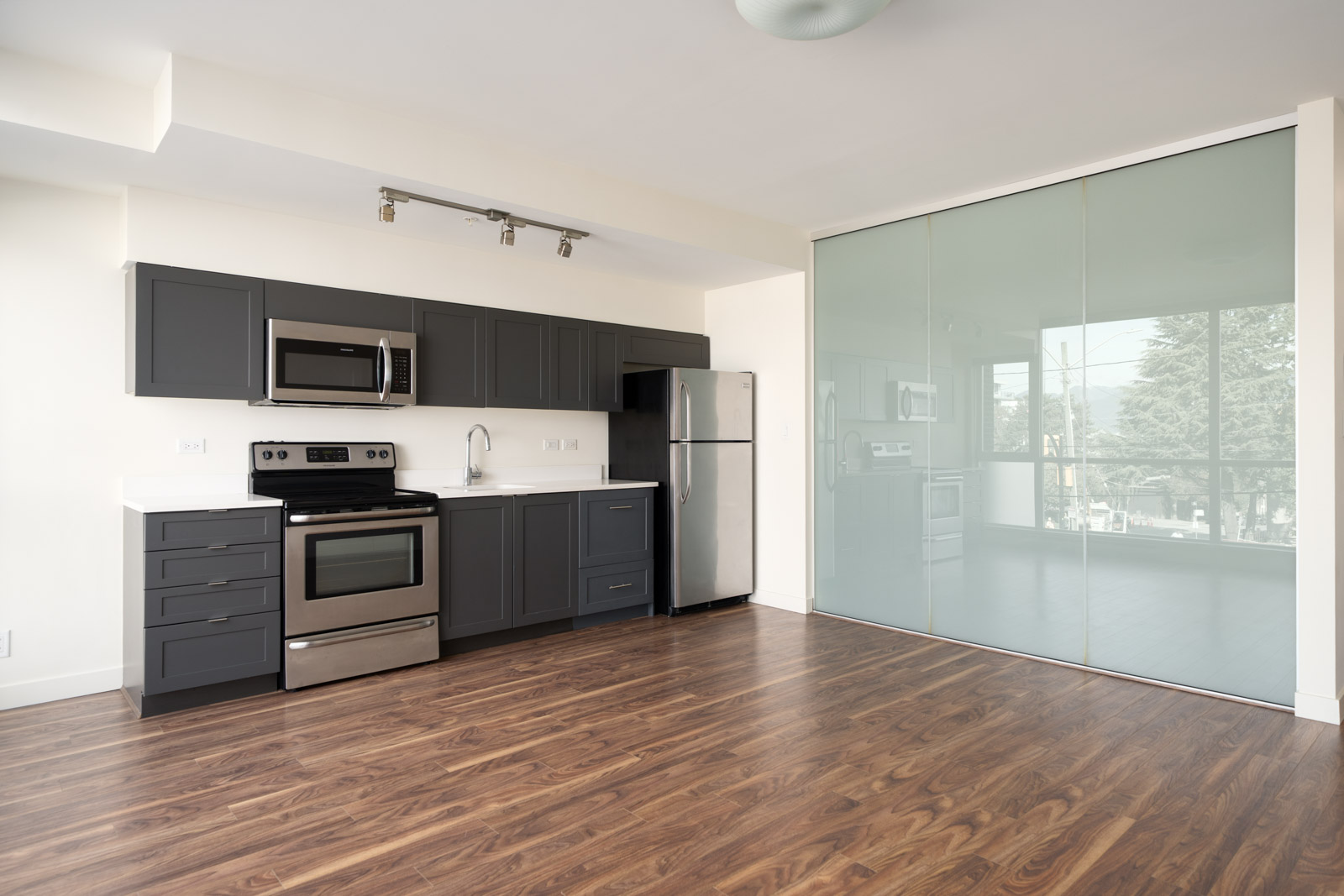 Modern kitchen in the 2511 Quebec office with dark grey cabinets, stainless steel appliances, and wood-look flooring.