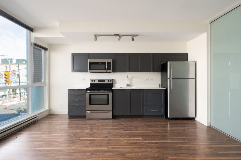 Modern kitchen with dark cabinets, stainless steel appliances, and wood flooring by floor-to-ceiling windows in Vancouver.