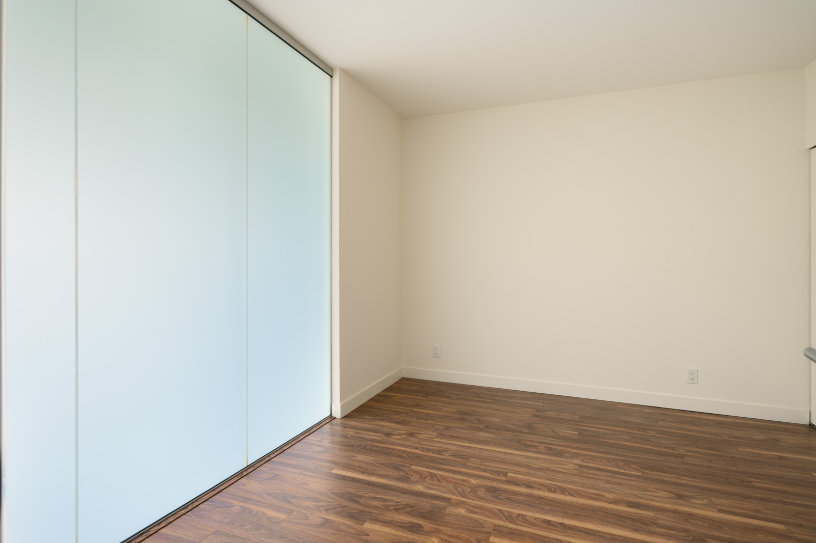 Empty office at 2511 Quebec with wood-look flooring, cream walls, and a large frosted glass sliding door.