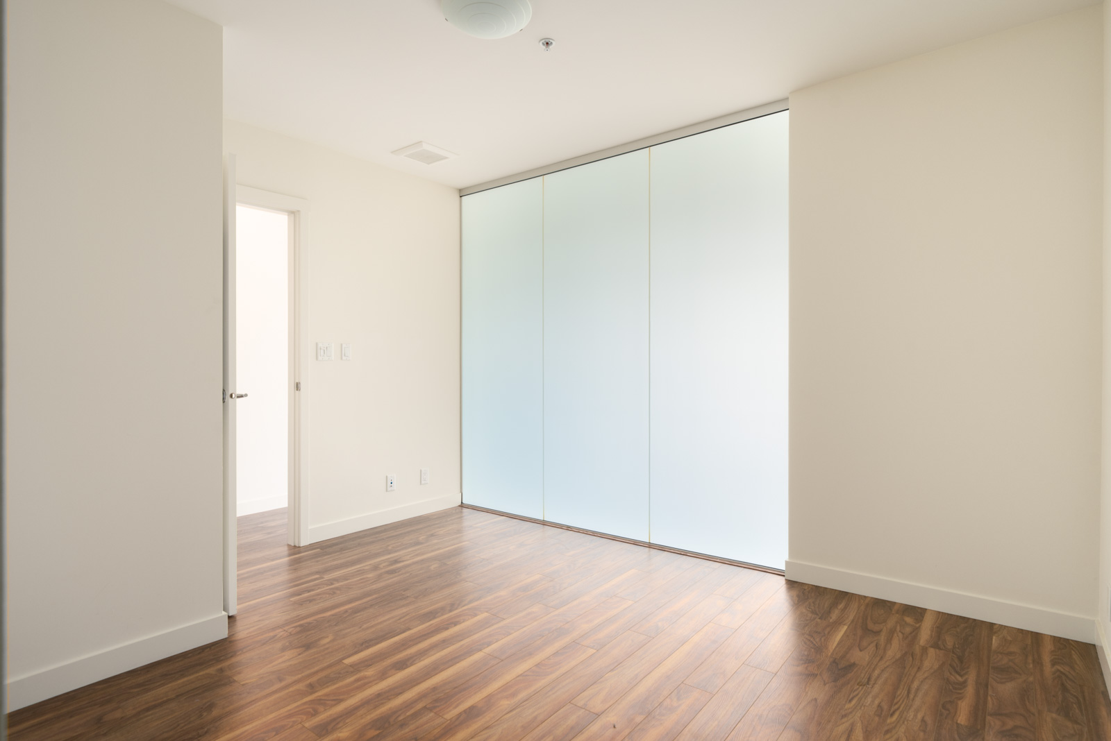Empty 2511 Quebec office with dark wood floors, an open doorway, and a wall of frosted glass panels.
