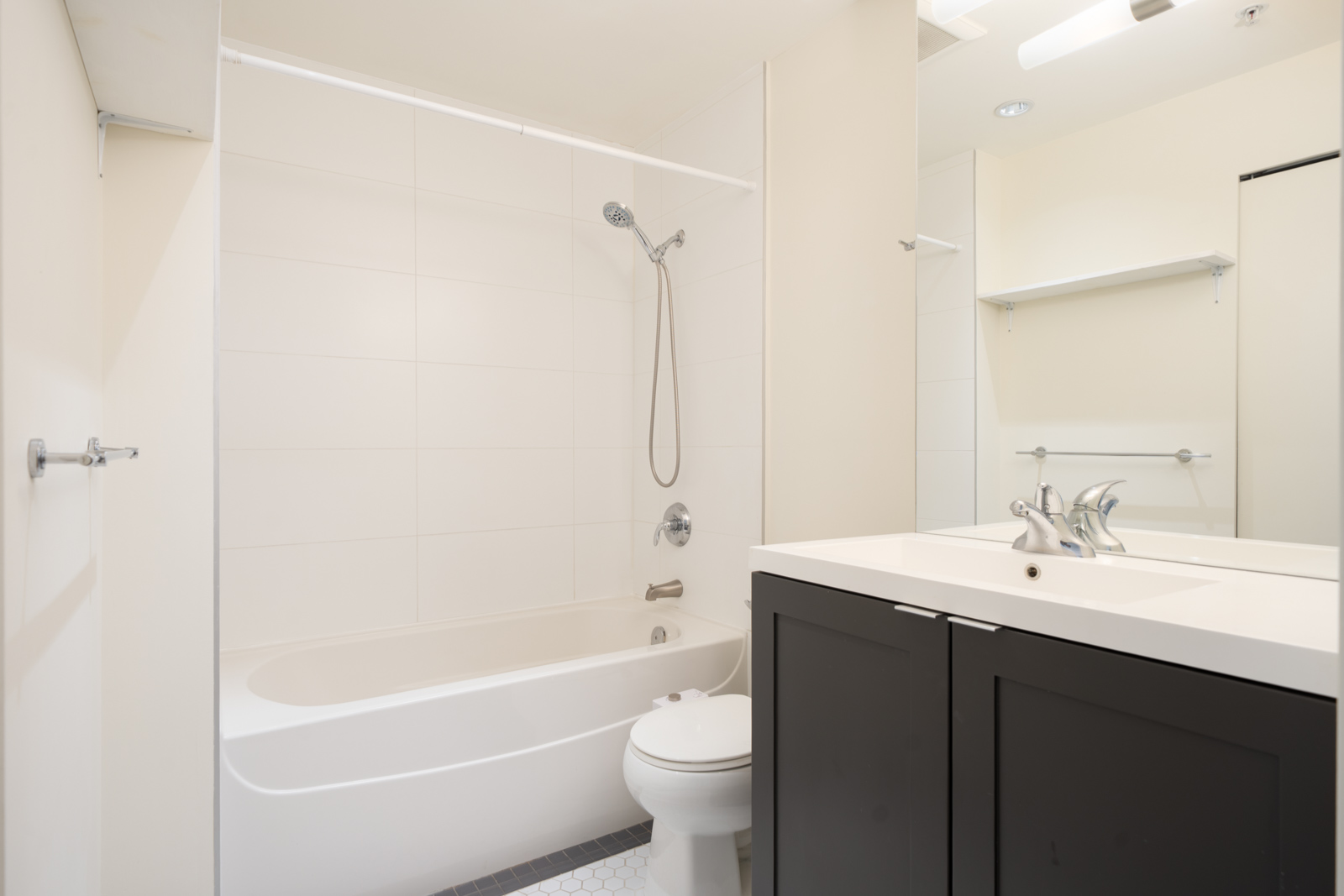 Bathroom at 2511 Quebec Street with a white tub, showerhead, toilet, and a vanity with a dark cabinet and white top.