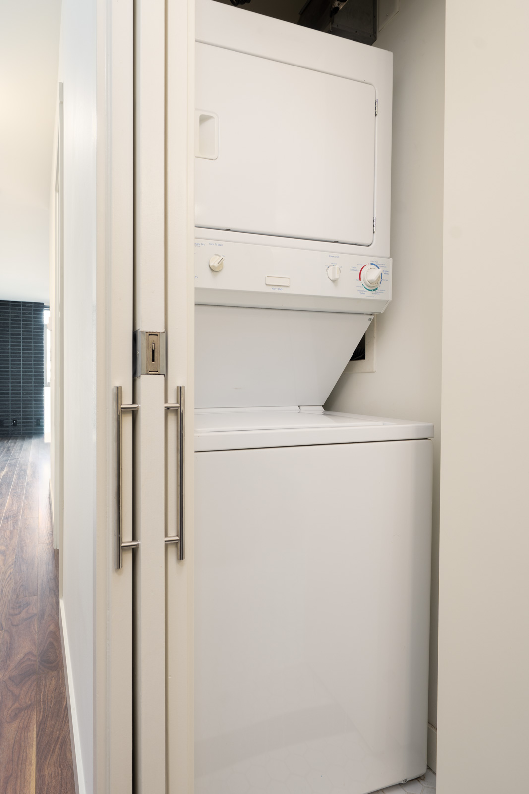 Stacked white washer and dryer in a 2nd floor office closet with bifold doors.
