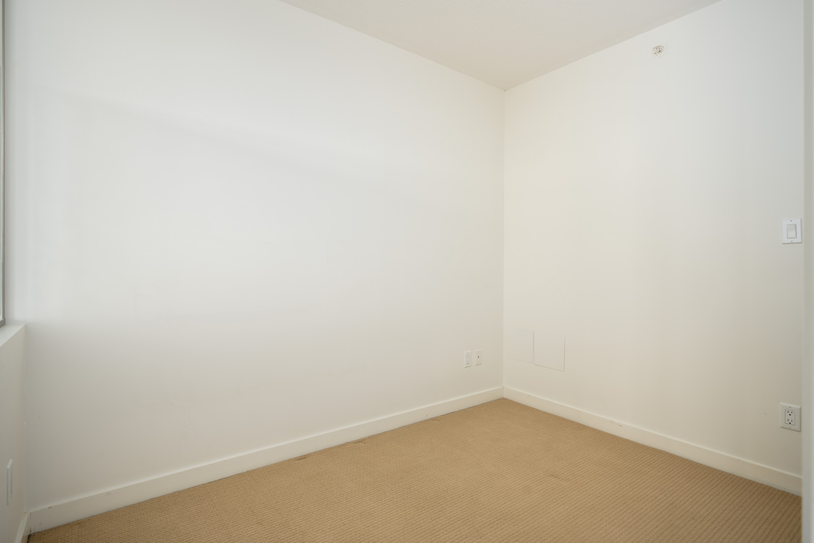 Empty corner of a Vancouver apartment featuring white walls and beige carpeting.