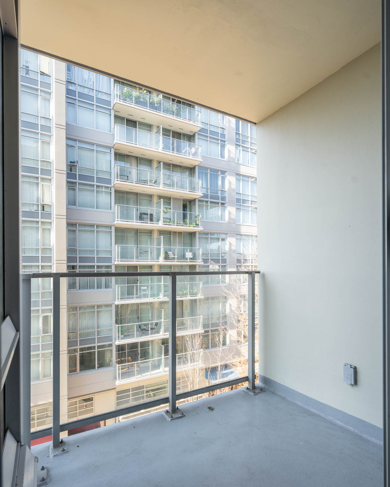View from a small apartment balcony looking toward a high-rise residential building with glass railings in Vancouver.